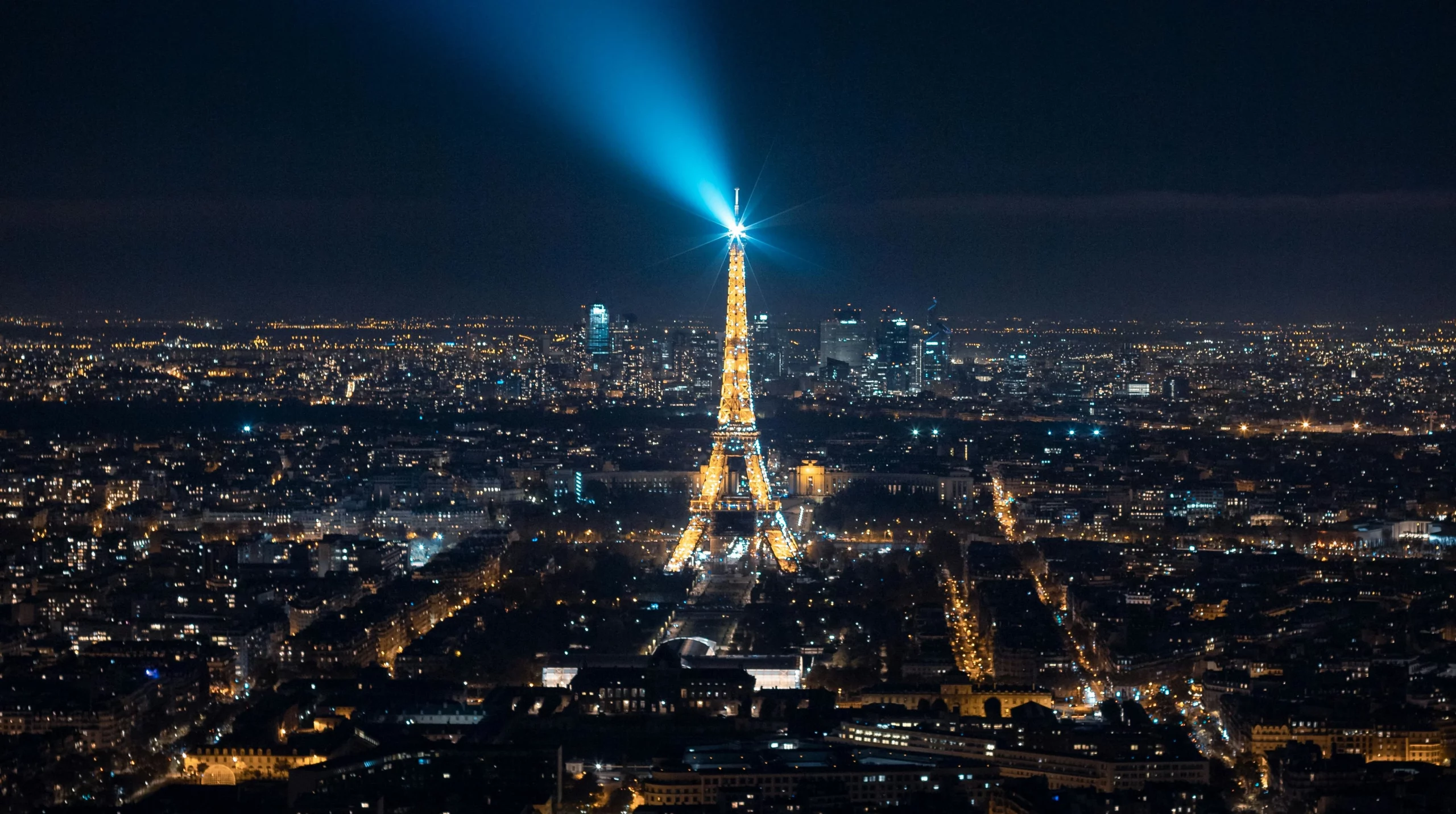 Una fotografía panorámica nocturna de Paris, con la torre Eiffel iluminada en el centro.